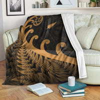 Dark blanket with gold koru and fern leaf pattern, draped over couch with white trim