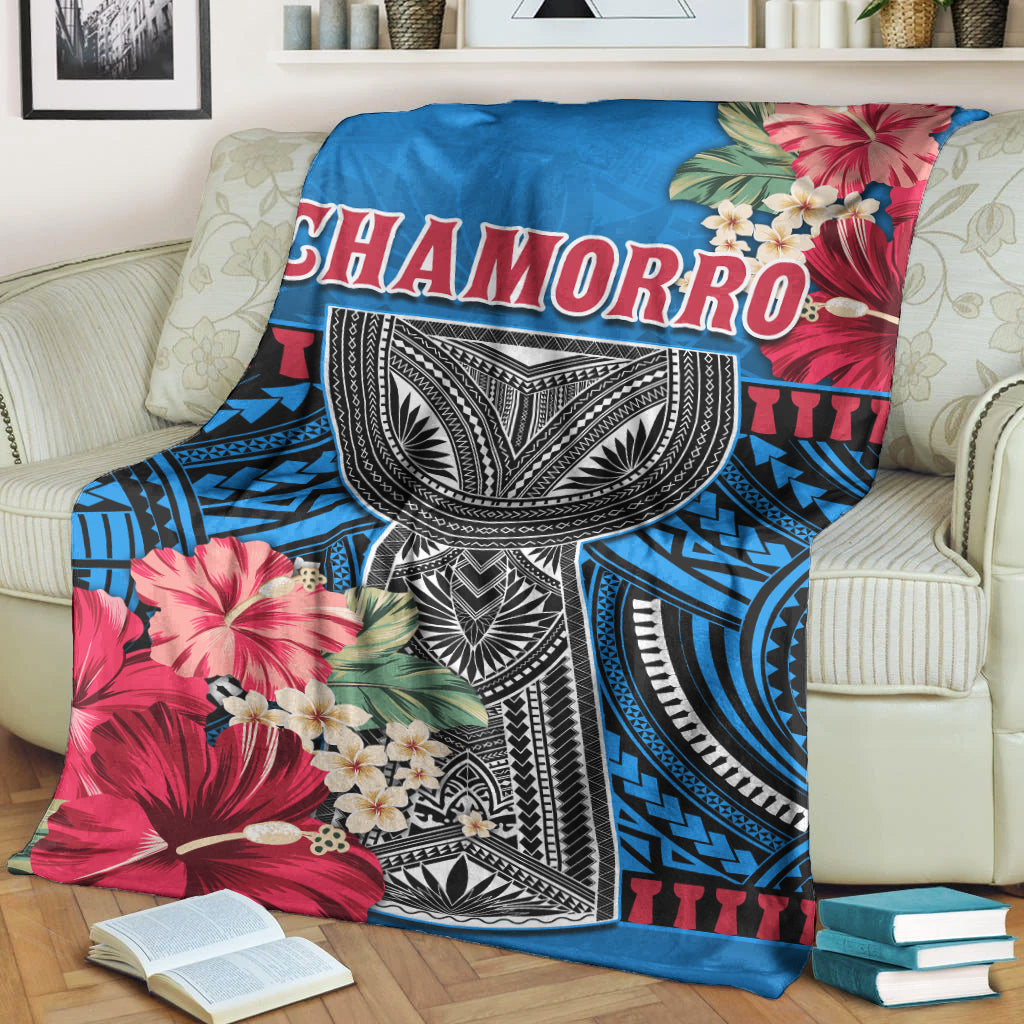 Blue CHAMORRO blanket draped on couch, showing hibiscus and white-black tribal design