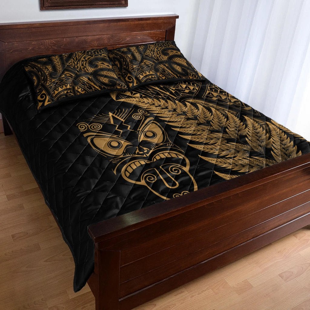 Black quilted bedspread corner with gold fern print and tribal mask emblem; 1 pillow shown