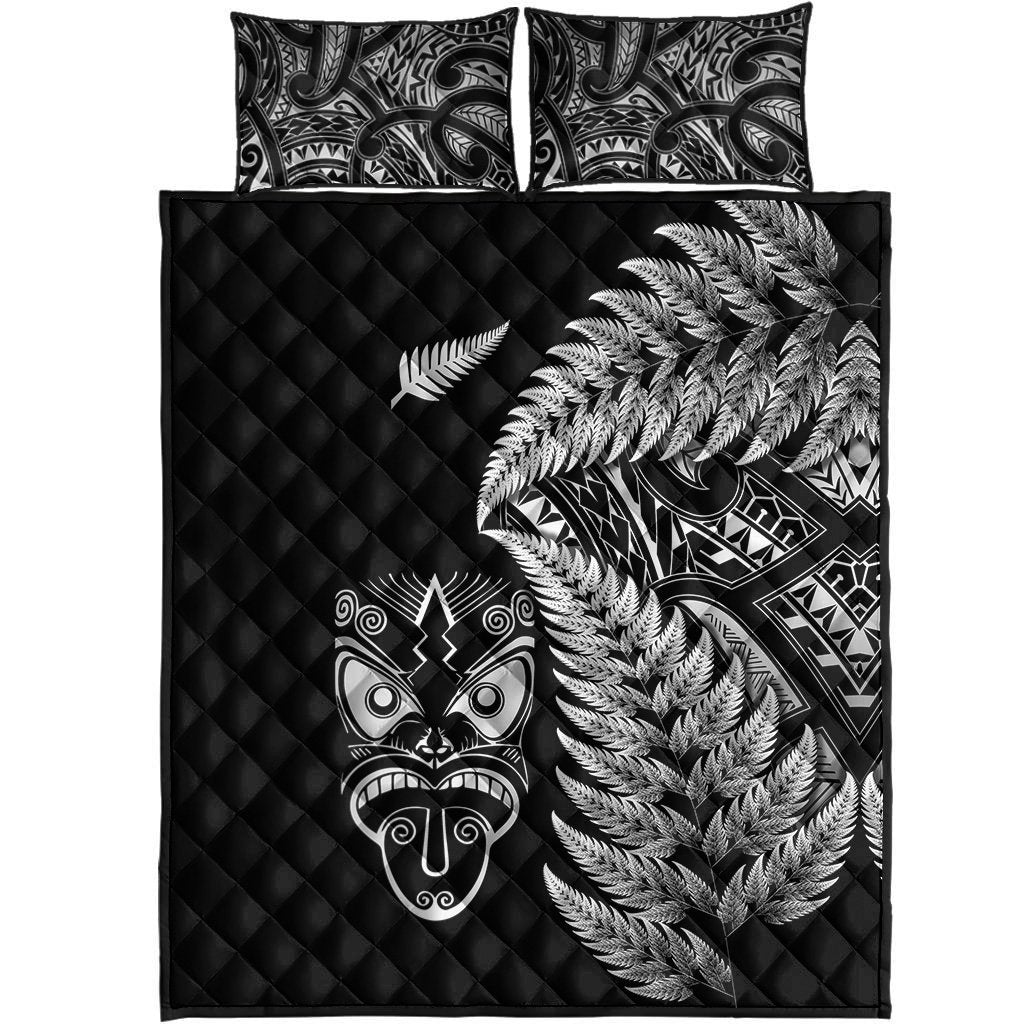 Front view: black quilt topper with silver fern and Maori mask motifs, two pillowcases