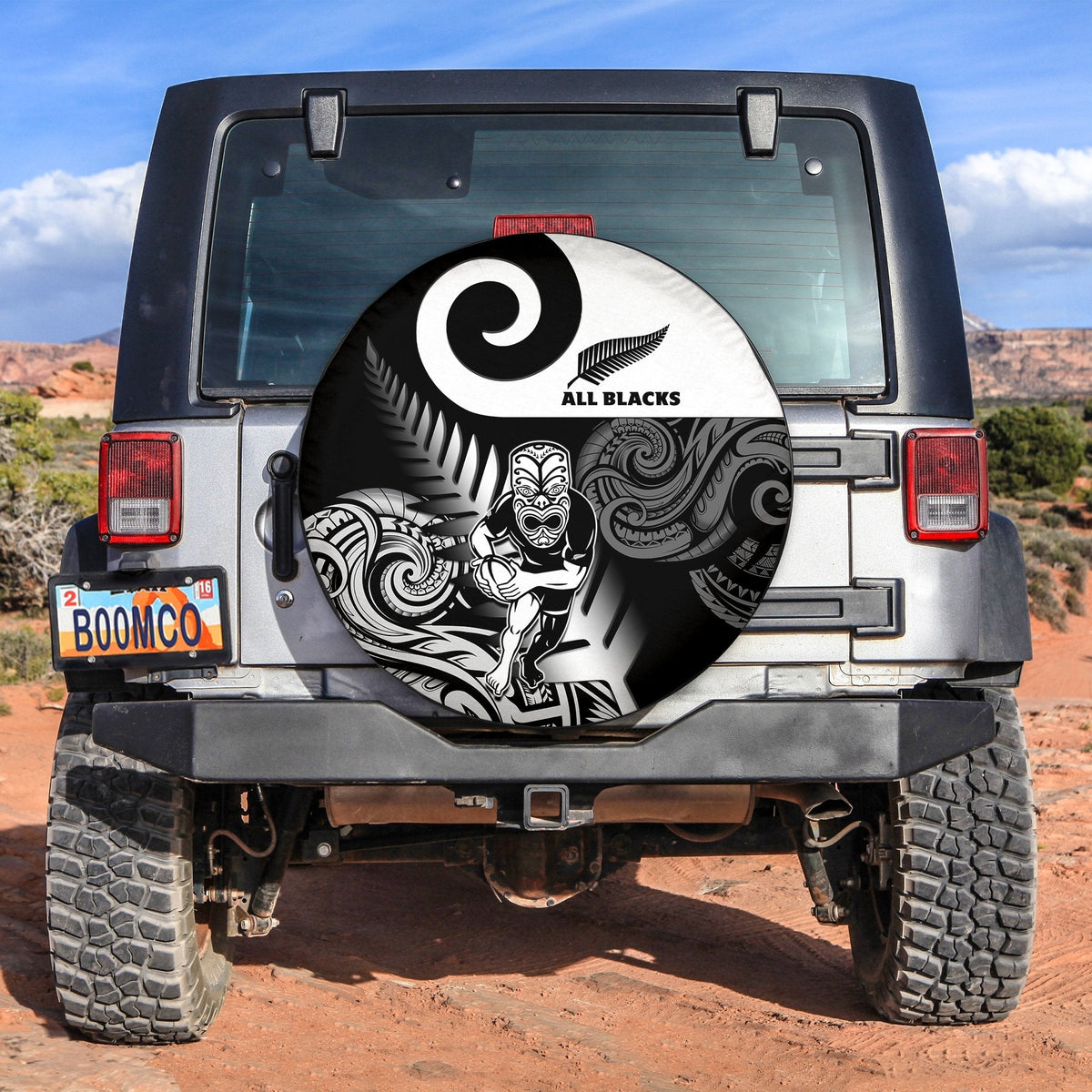 Circular black spare tire cover with white All Blacks logo and fern-spiral tribal pattern