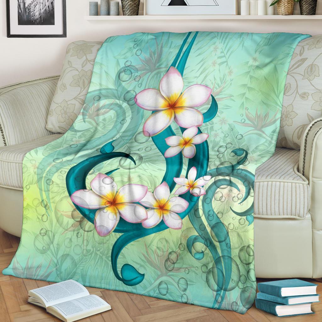 Hawaii plumeria blanket draped on couch, teal and green with white blossoms and vines.