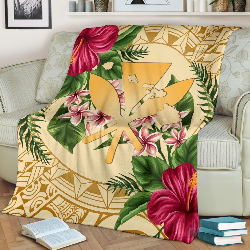 Gold Hawaiian blanket draped on sofa; hibiscus and plumeria flowers with palm leaf motifs