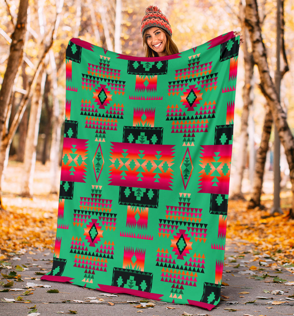 Light green geometric blanket with tribal-inspired native pattern held up outdoors