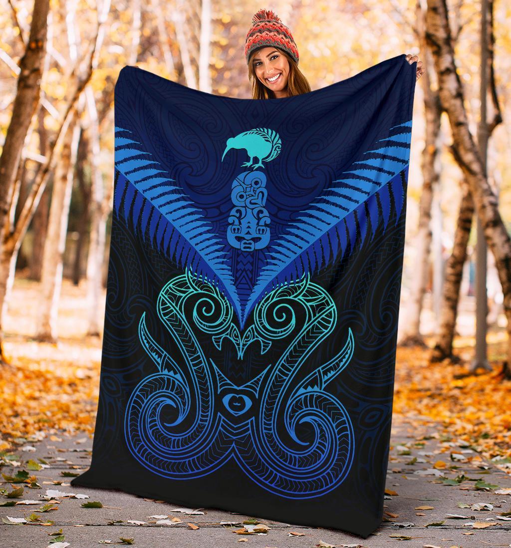 Blue Maori manaia blanket with teal and black tribal wings pattern, held outdoors