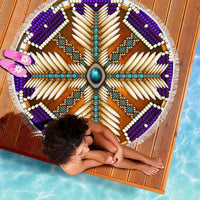 Top view of round beach blanket: purple and brown mandala rays, turquoise center, white fringe