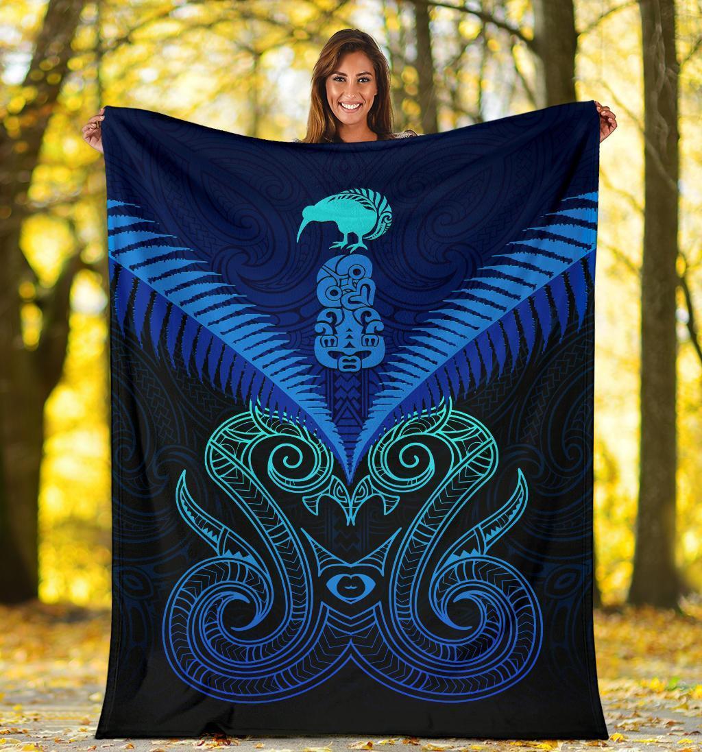 Blue Maori manaia blanket with teal face and swirl motifs, held up outdoors
