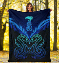 Blue Maori manaia blanket with teal face and swirl motifs, held up outdoors