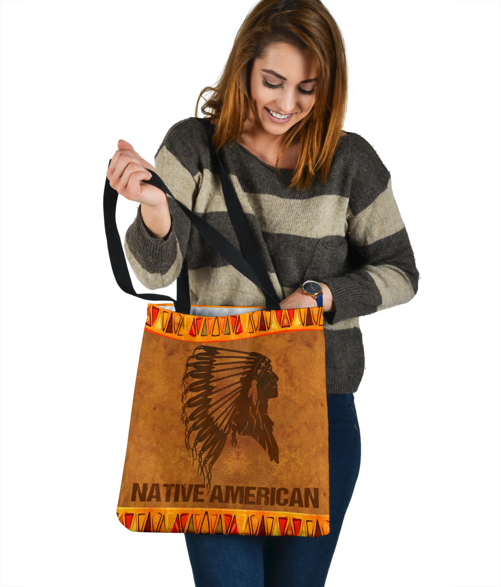 Brown tote bag with black headdress print, orange tribal border, and centered Native American wording
