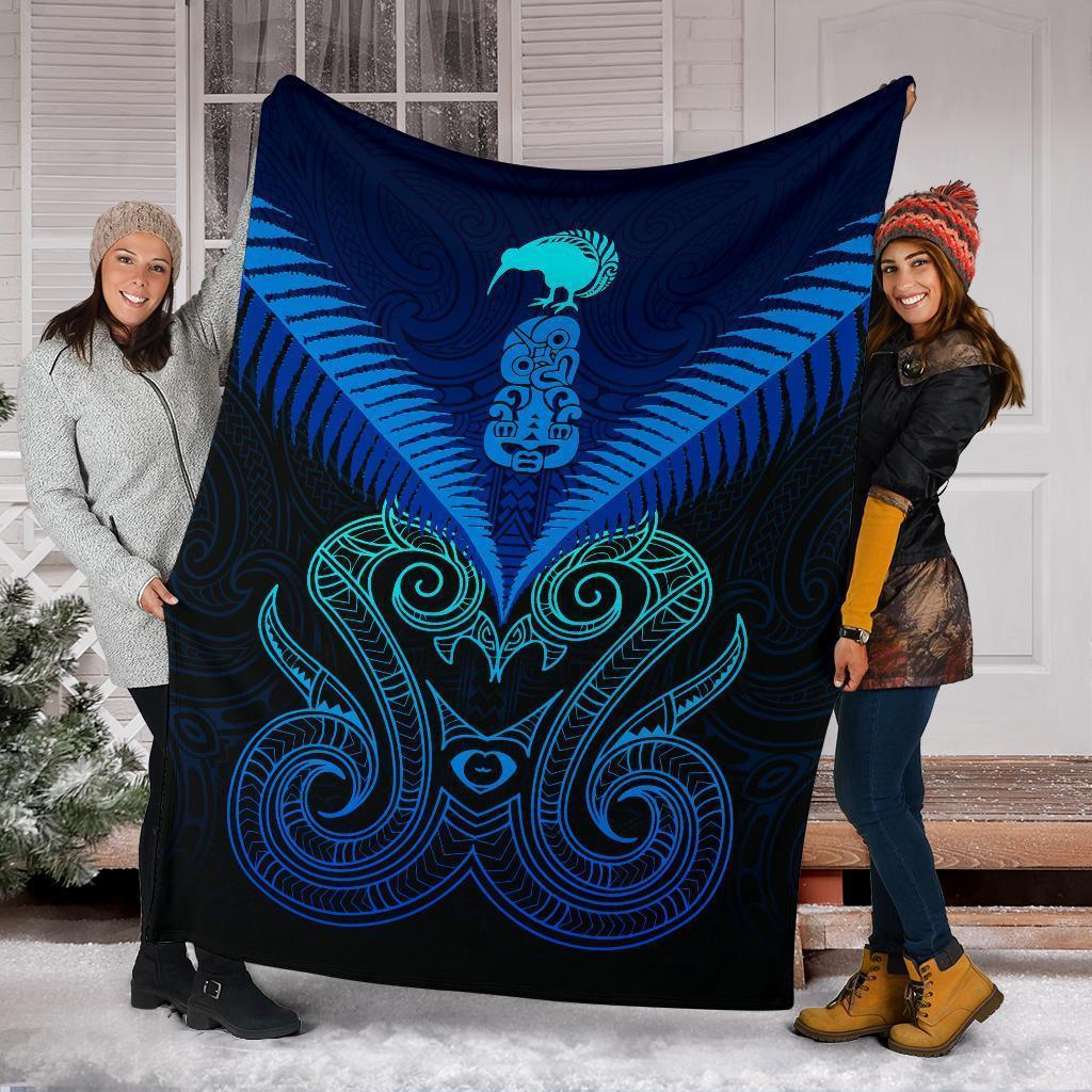 Blue Maori manaia blanket with teal tribal design, held by two people indoors