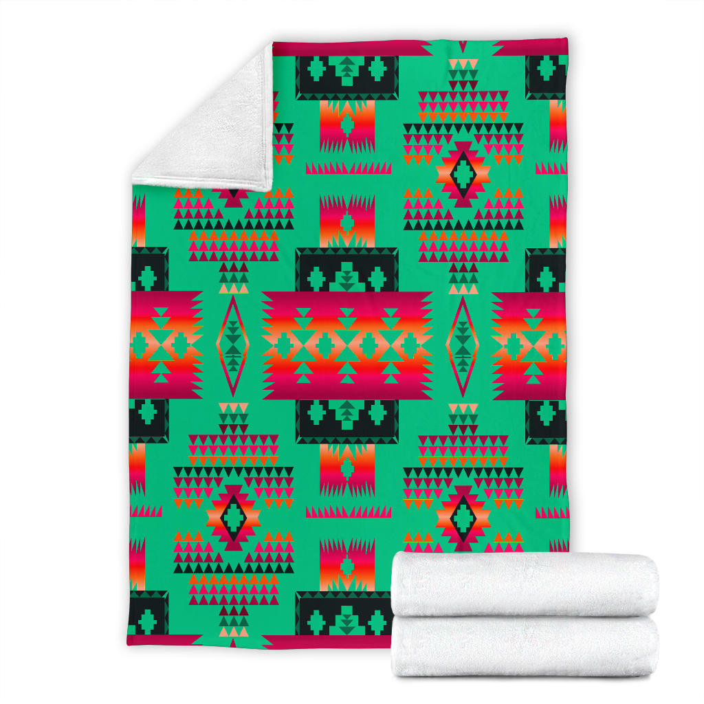 Light green geometric blanket with tribal pattern, folded and stacked with two rolled towels