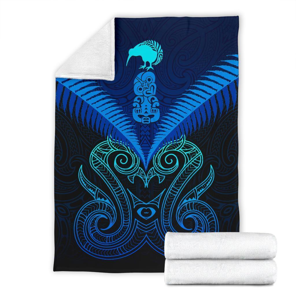 Folded blue Maori manaia blanket with teal swirl pattern and rolled matching fabric