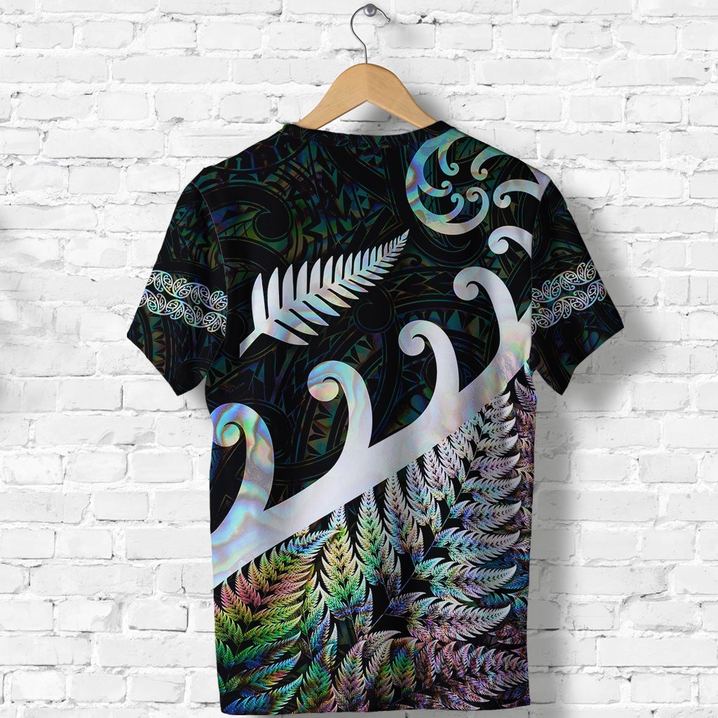 Dark green T-shirt with white fern-and-koru design across front, colorful feather pattern